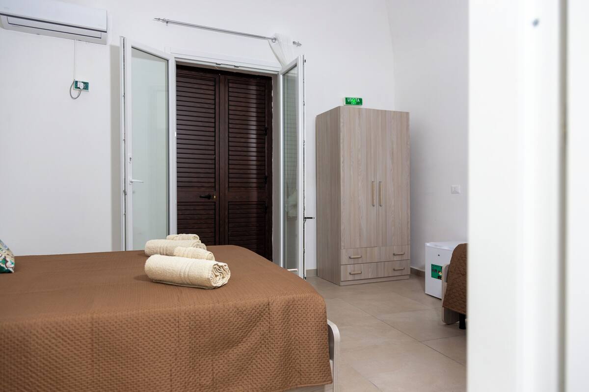 A hotel room with a bed, a wardrobe, and a small cabinet.