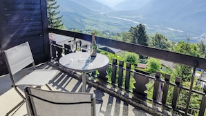 A balcony with a table and chairs, a bottle of champagne, and a scenic mountain view. - Sans Nom by Interhome (Crans-Montana)