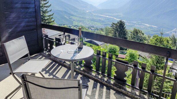 Een balkon met een tafel en stoelen, een champagnefles en een schilderachtig uitzicht op de bergen.