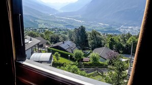 Uitzicht vanuit een raam op een vallei met bergen, huizen en een rivier.