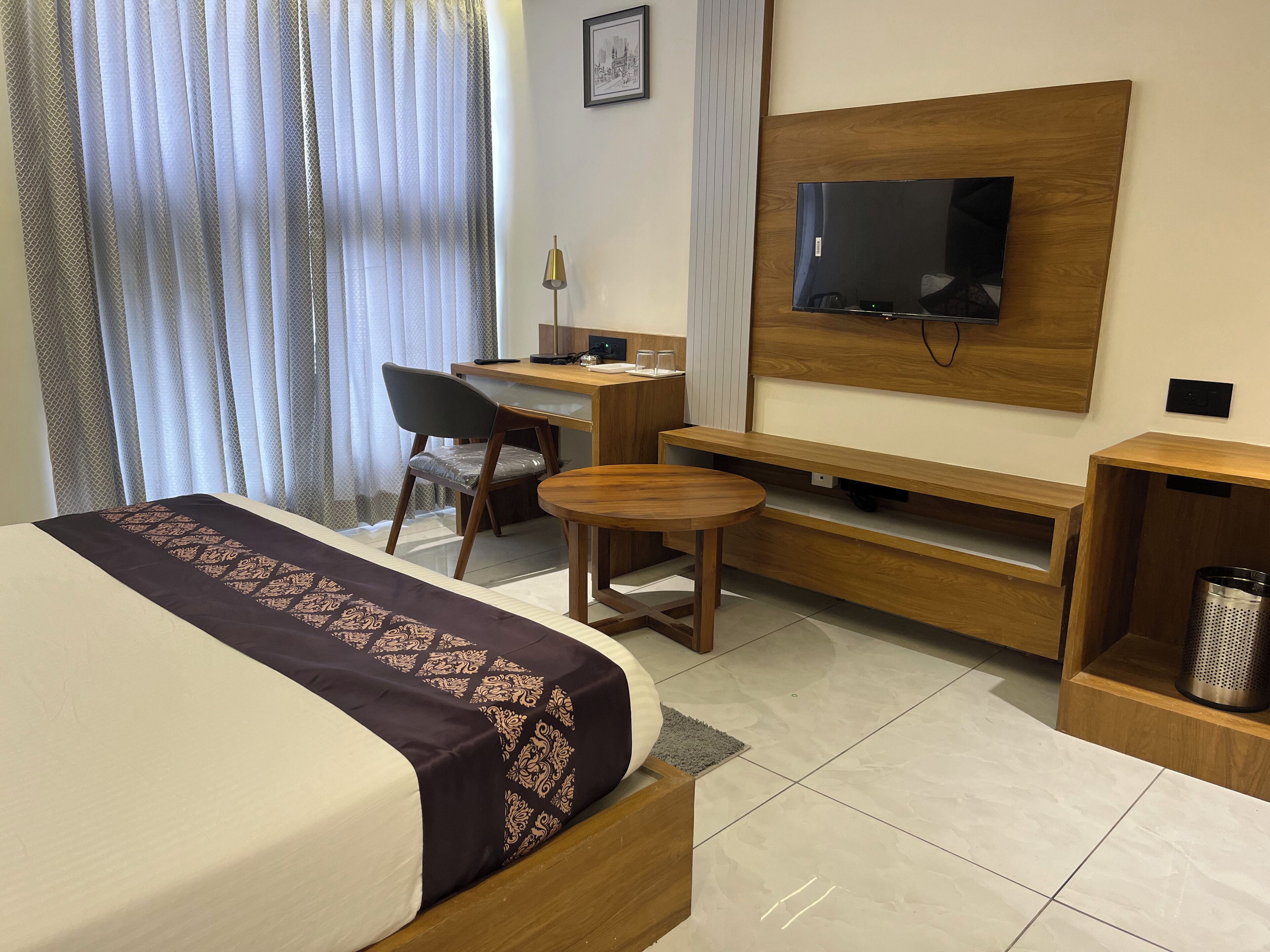 Ein Hotelzimmer mit einem Bett, einem Schreibtisch, einem Stuhl, einem an der Wand montierten Fernseher und einem kleinen Tisch.