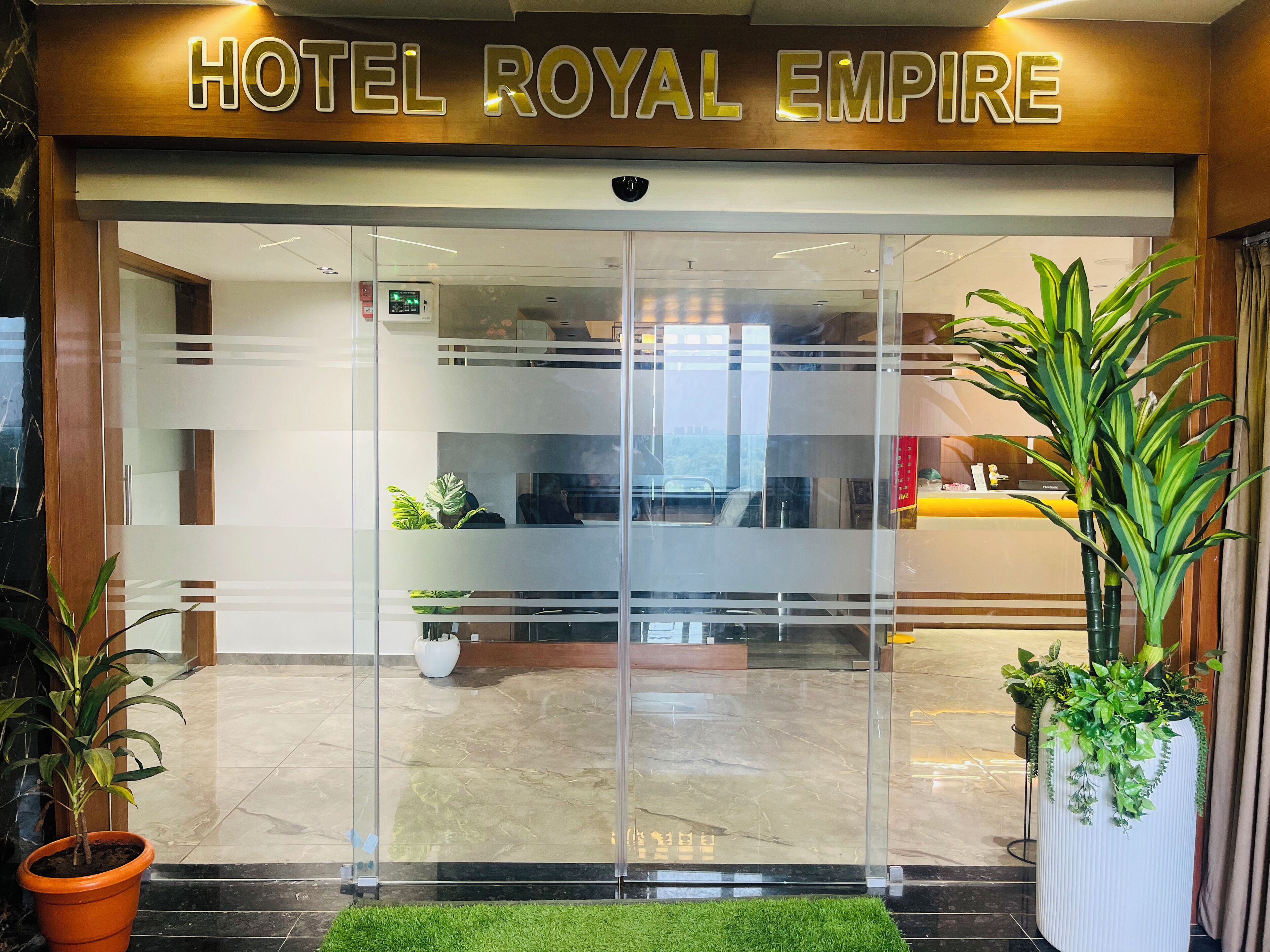La entrada del Hotel Royal Empire, con una recepción, puertas de vidrio y plantas en macetas.