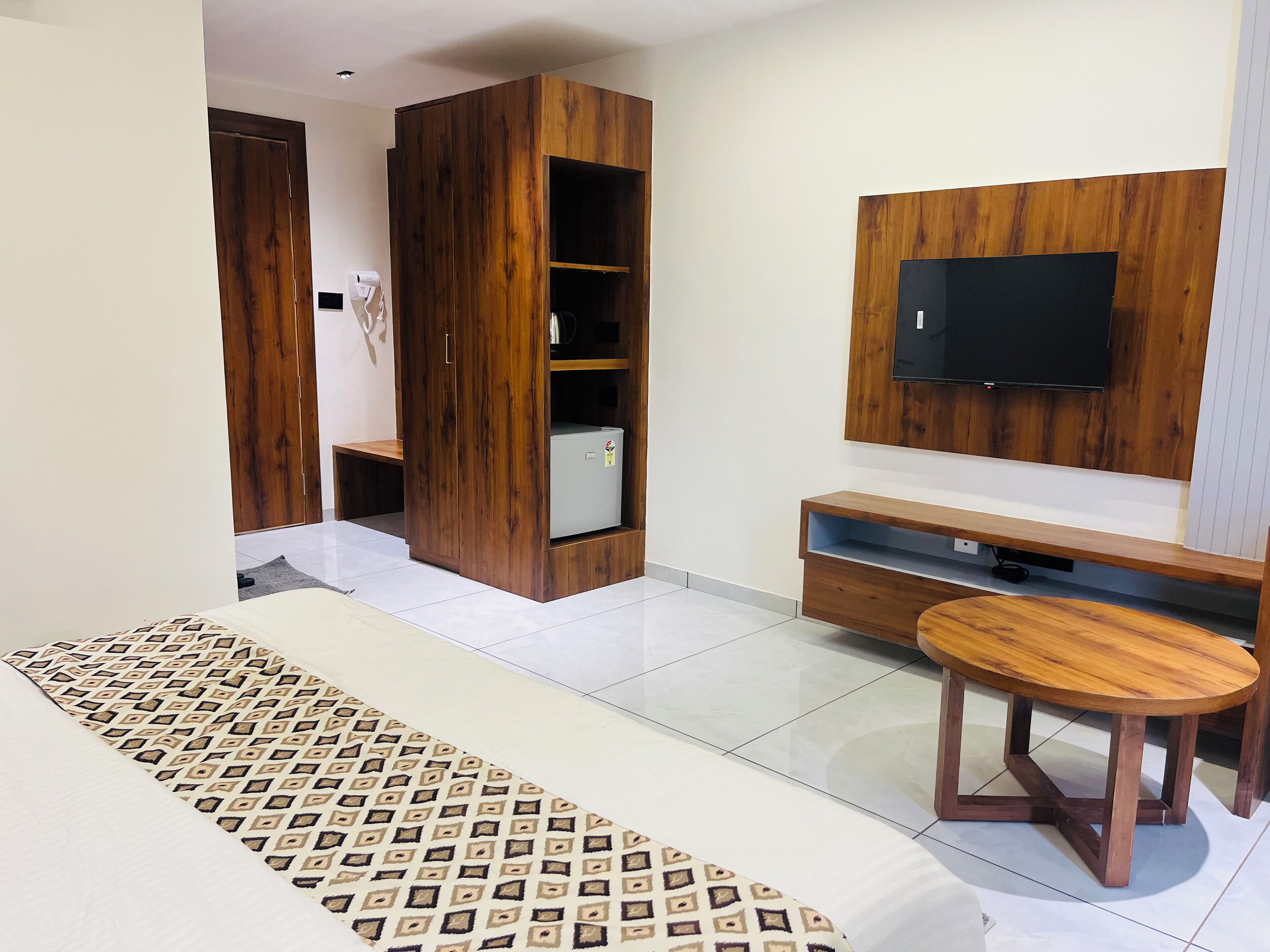 A modern bedroom with a bed, a wooden wardrobe, a TV, and a small wooden table.