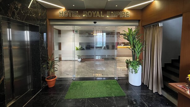 Hotel Royal Empires indgang med et moderne design, der inkluderer en receptionsdisk, potteplanter og en glasdør.
