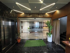 La entrada del Hotel Royal Empire, con un diseño moderno, que presenta una recepción, plantas en macetas y una puerta de cristal.