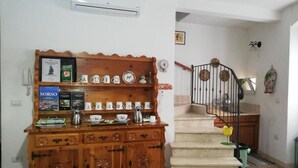 Un mueble de madera con platos decorativos y una cafetera, una escalera con barandilla metálica y un aire acondicionado instalado en la pared.