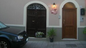 Un edificio de dos pisos con una puerta marrón oscuro, fachada de color claro y una pequeña ventana con contraventanas.