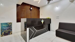 Zona de recepción con un mostrador negro, una pared de acento de madera, un ventilador de techo y un letrero anunciando la gran inauguración de TRANQUIL INN.