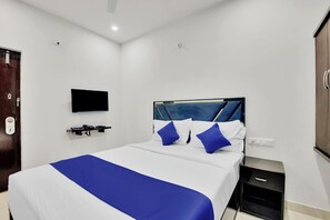 Une chambre d’hôtel moderne avec un grand lit, un téléviseur à écran plat fixé au mur, une armoire en bois et une petite table de chevet.