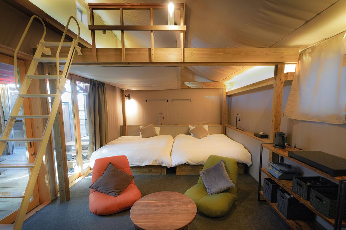 A cozy, well-lit room with a loft bed, a small table, two chairs, and a ladder.