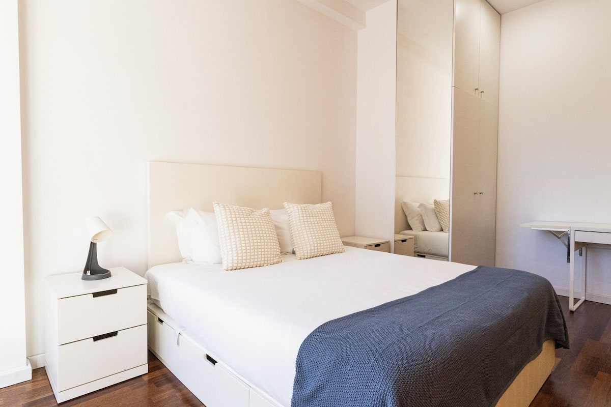 A bedroom with a bed, bedside tables, a desk, and a mirror.
