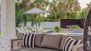 Zona d'estar exterior moderna amb un sofà, dues begudes sobre una taula i un espai relax a la piscina amb ombrelles.