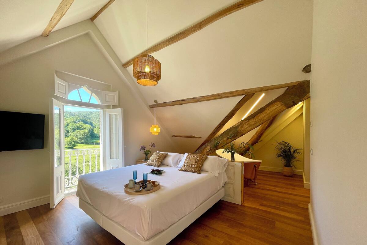 Ein Schlafzimmer mit einem großen Bett, Holzbalken, einem Fernseher und einem Balkon mit Blick.