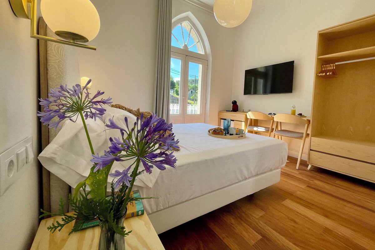 Ein Hotelzimmer mit Bett, Schreibtisch, Stuhl, Fernseher und einem Fenster mit Vorhängen.
