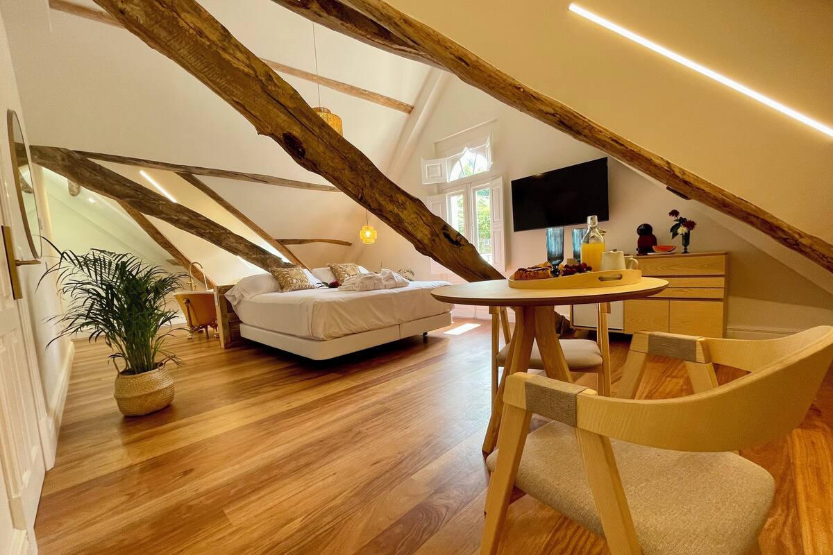 Ein modernes Schlafzimmer im Loft-Stil mit Holzbalkendecke, einem Bett, einem Esstisch und einem Fernseher.