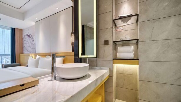Une salle de bain d’hôtel moderne, dotée d’un grand miroir, d’un lavabo rond et d’une douche intégrée.
