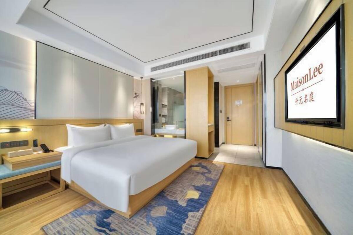 Ein modernes Hotelzimmer mit einem großen Bett, Nachttischen, einem Spiegel und einem an der Wand befestigten Fernseher.
