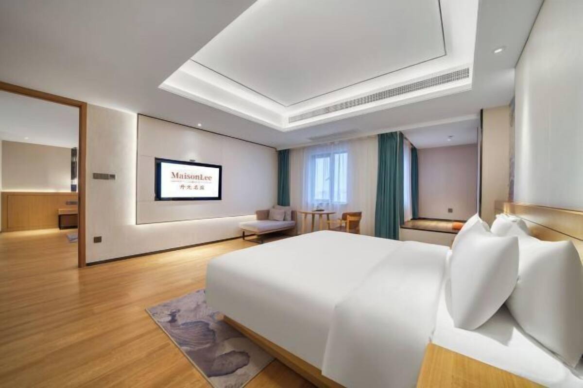 Ein Hotelzimmer mit Bett, Schreibtisch, Stuhl, Sofa, einem kleinen Tisch und einem an der Wand befestigten Fernseher.
