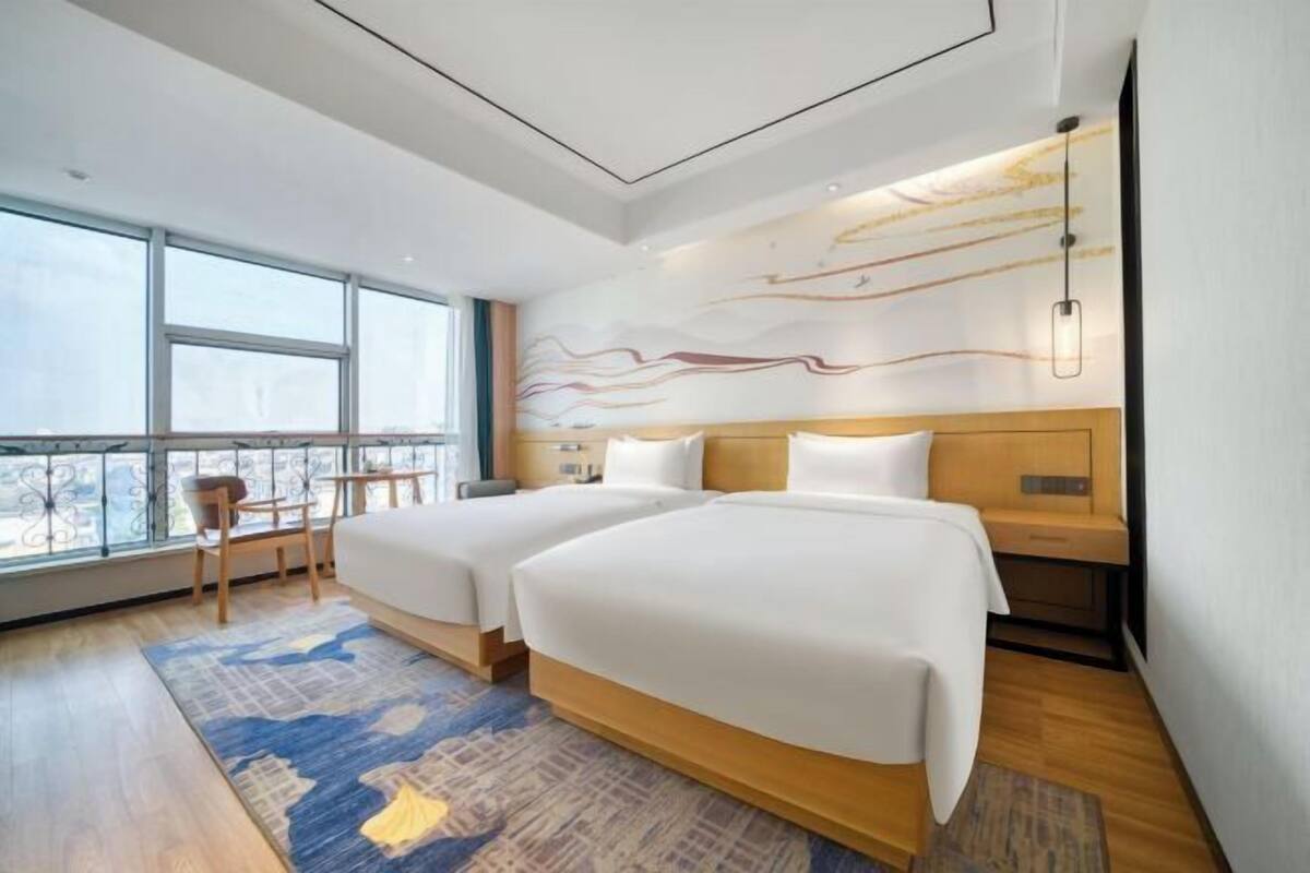 Ein Hotelzimmer mit zwei Betten, einem großen Fenster, Blick auf die Stadt und modernem Design.