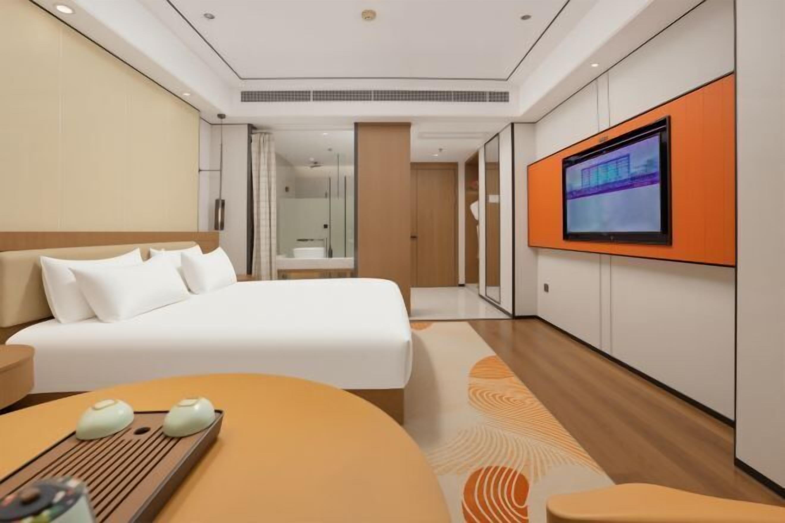 Ein modernes Hotelzimmer mit einem Bett, einem an der Wand montierten Fernseher und einem kleinen Tisch mit Tablett.