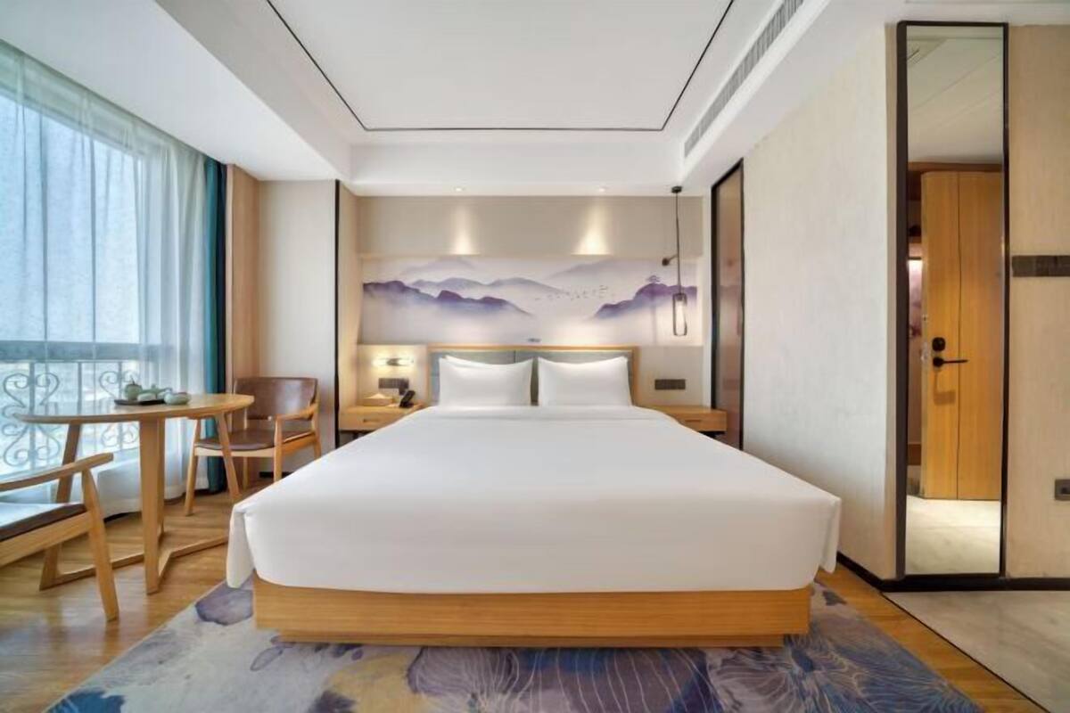 Ein Hotelzimmer mit einem großen Bett, einem Schreibtisch mit Stuhl, einem kleinen Tisch und Blick ins Freie durch das Fenster.