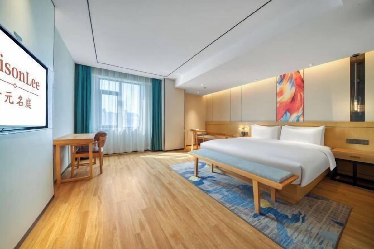 Ein modernes Hotelzimmer mit Bett, Nachttisch, Sessel und einem großen Fenster mit Vorhängen.