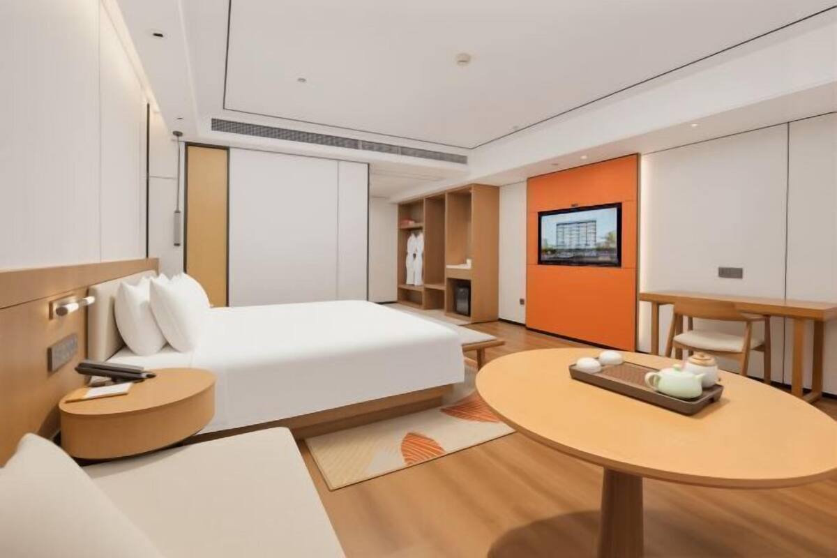 Ein modernes Hotelzimmer mit Bett, Nachttisch, rundem Tisch mit Tee-Service und einem an der Wand befestigten Fernseher.