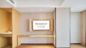 Une chambre d’hôtel avec un plancher en bois, un banc, un téléviseur fixé au mur et une armoire en bois.