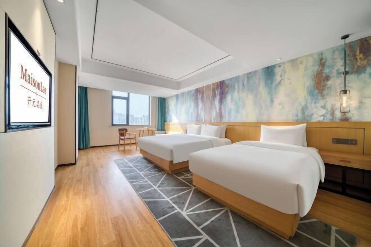 Ein Hotelzimmer mit zwei Betten, einem Schreibtisch, einem Stuhl und einem großen, abstrakten Gemälde an der Wand.