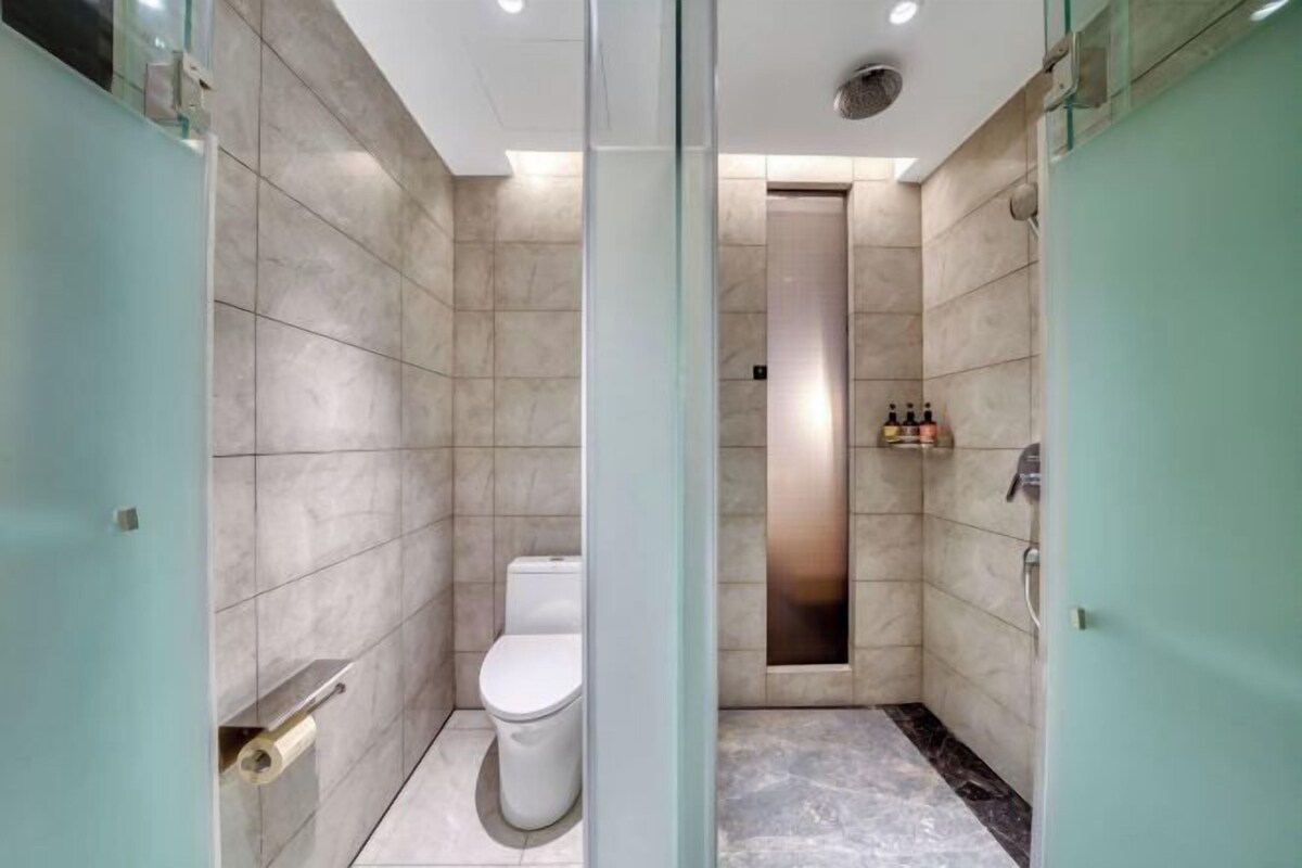 A modern bathroom with a toilet, shower, and glass partition.