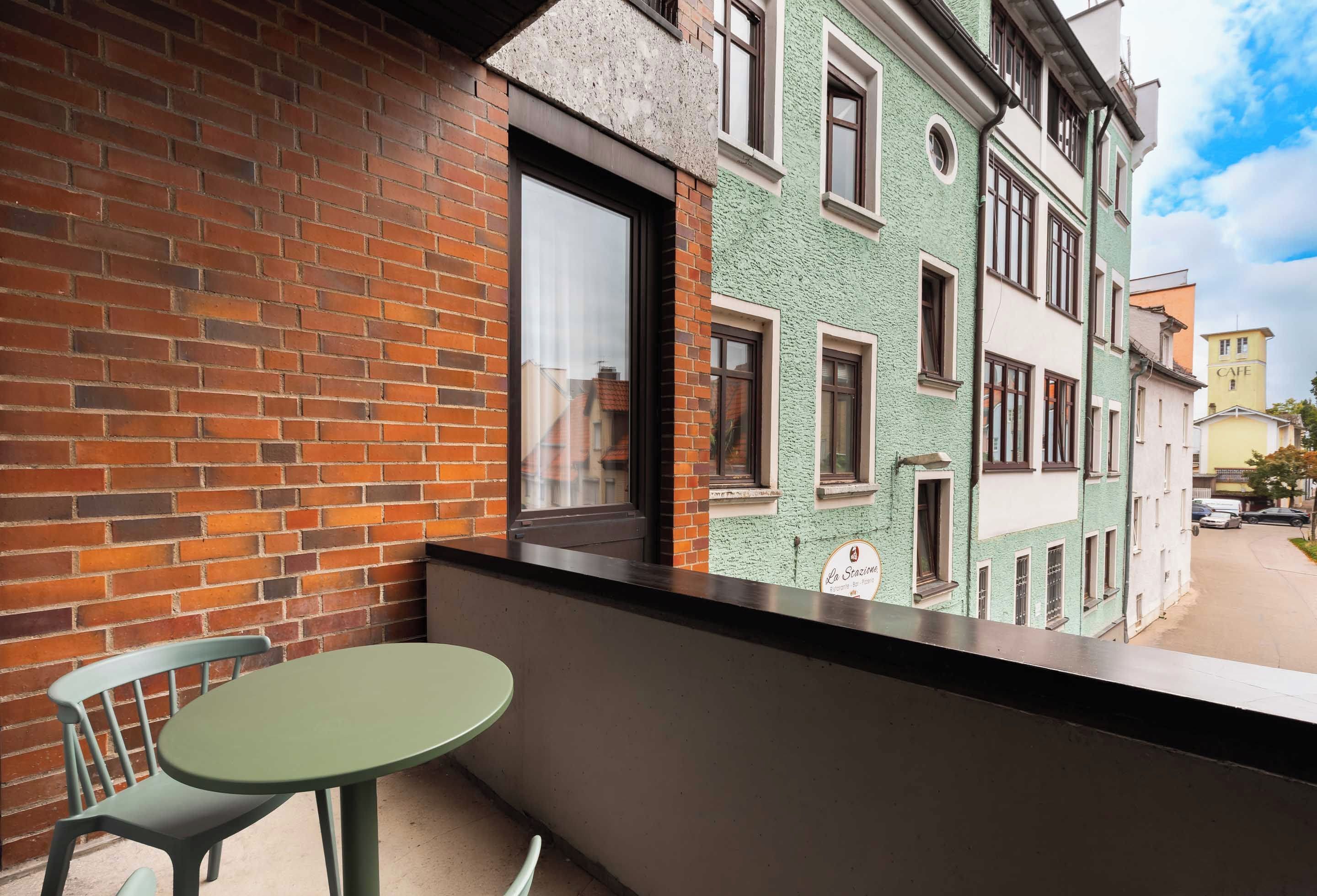 A balcony with a brick wall, a window, and a table with a chair.