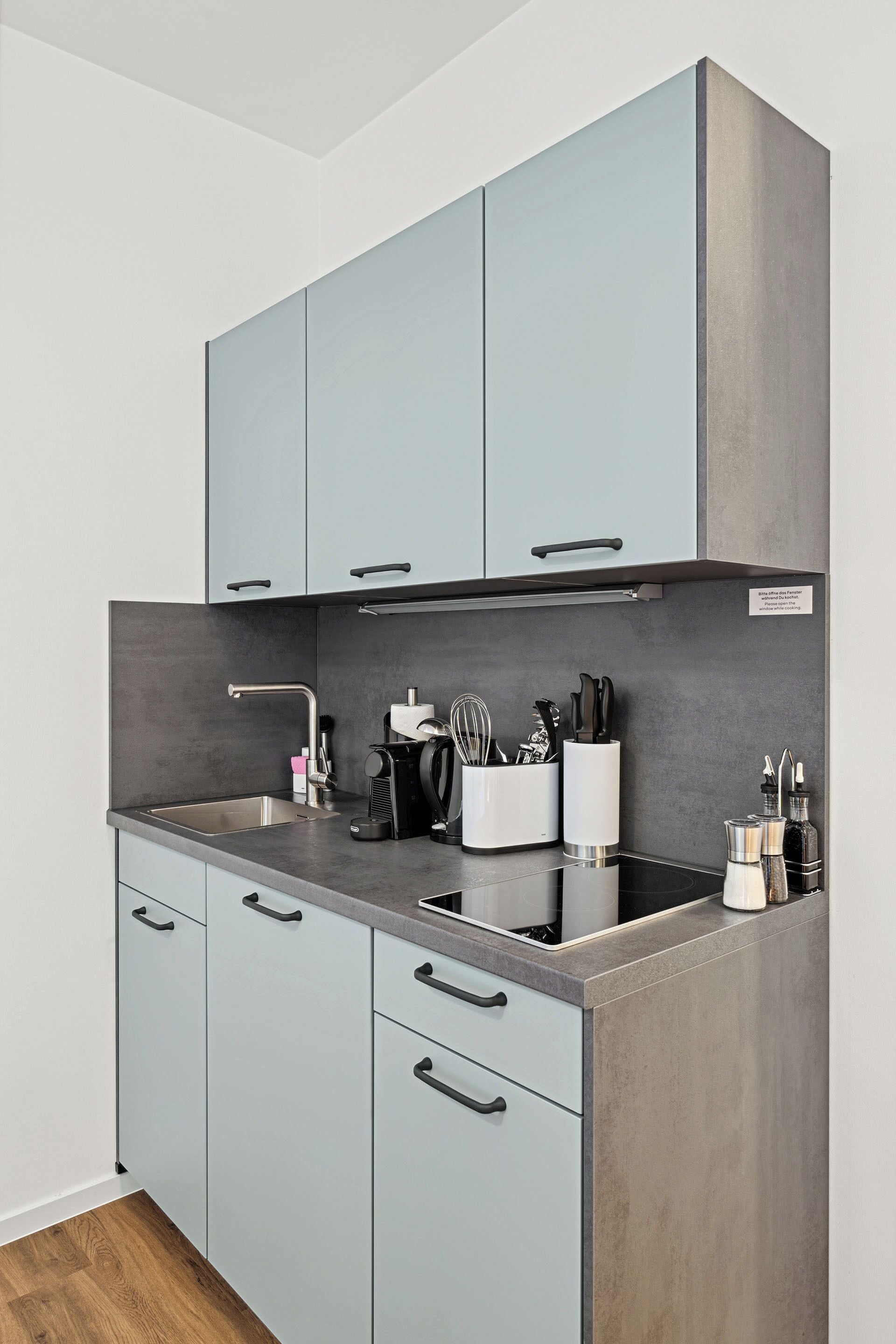 Une cuisine moderne avec des meubles gris, un évier en acier inoxydable et un plan de travail noir.