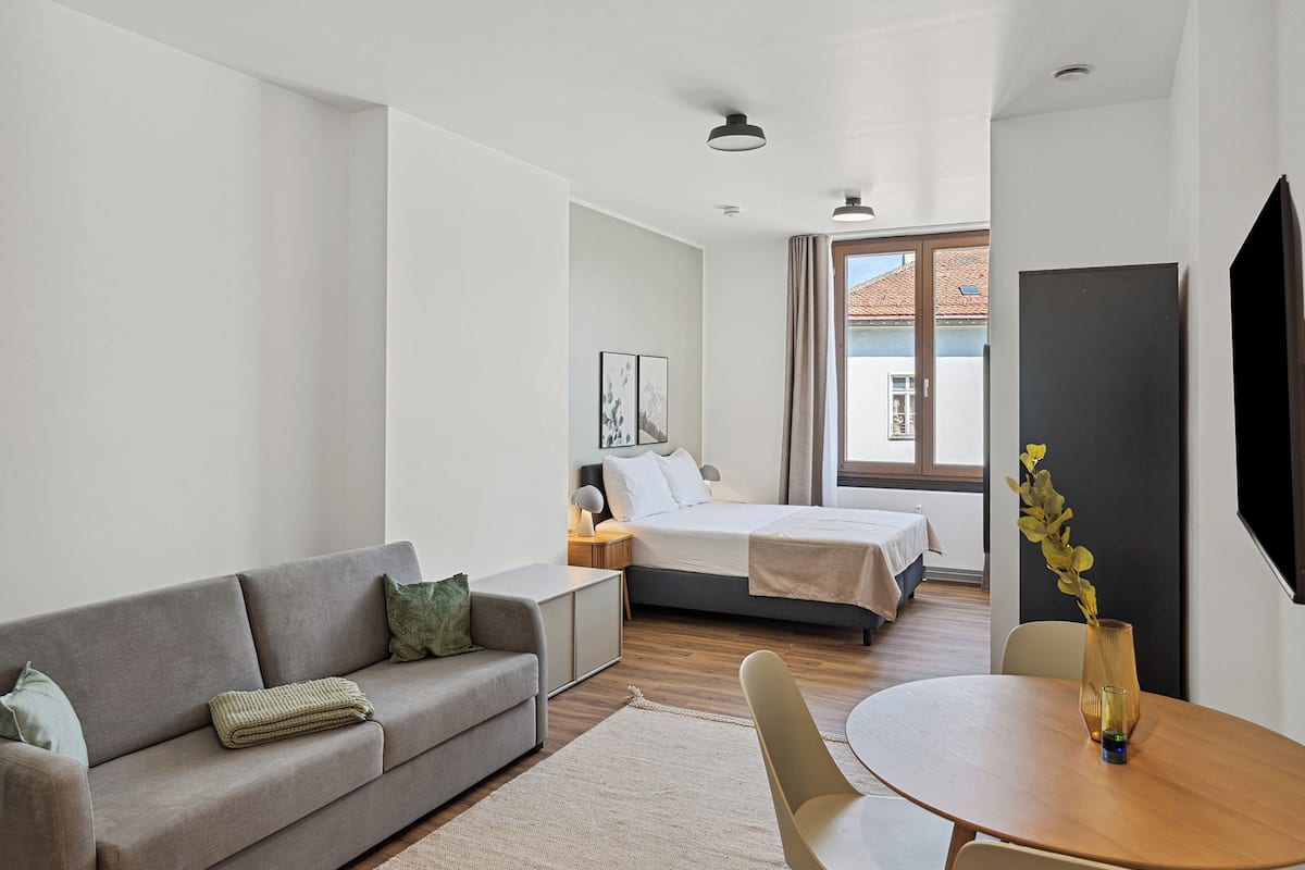 Una habitación de hotel moderna con sofá, cama, mesa de comedor y televisión.
