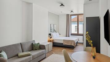 A modern hotel room with a sofa, a bed, a dining table, and a TV.