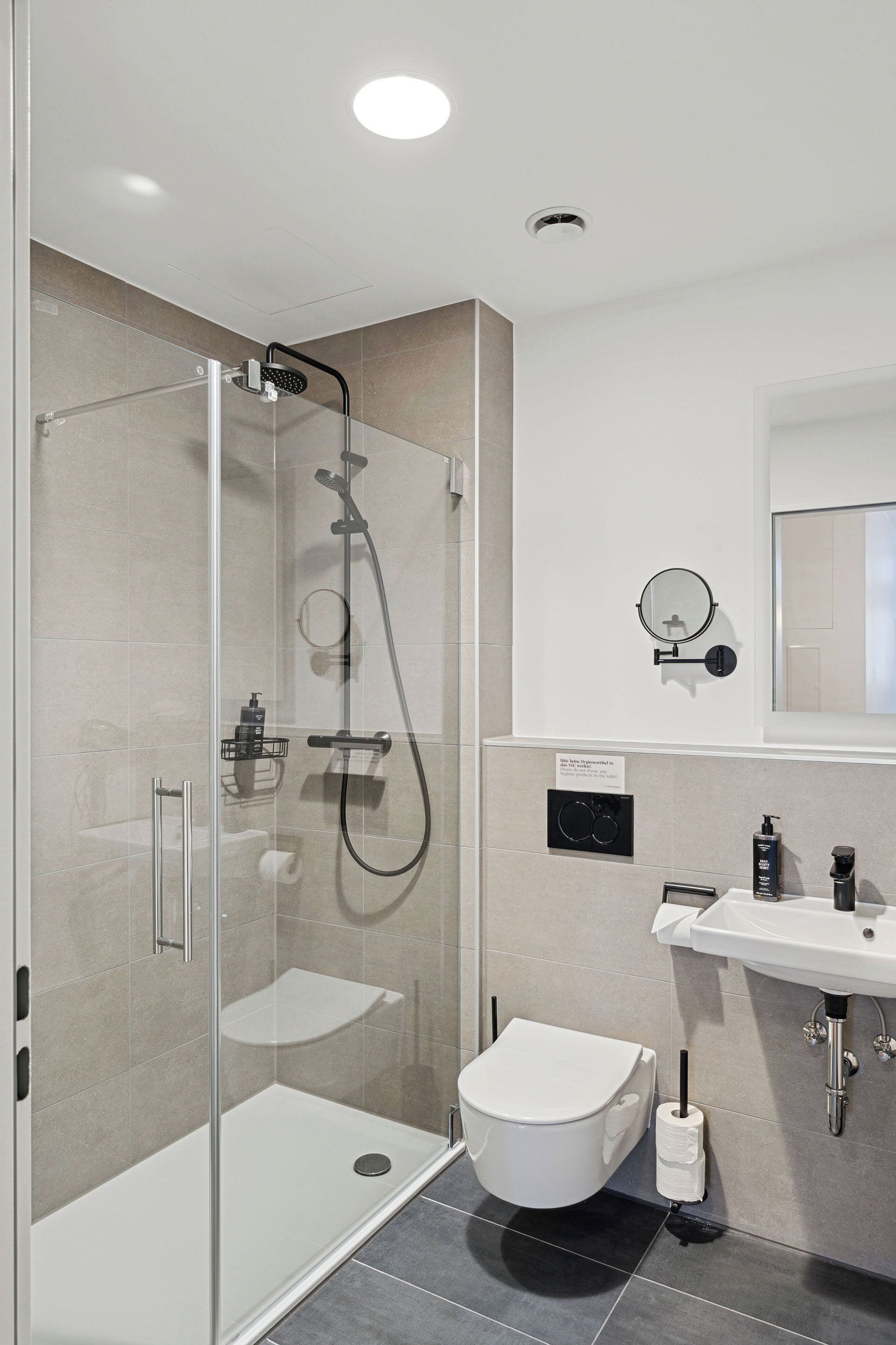 A modern bathroom with a glass-enclosed shower, a toilet, a sink, and a mirror.