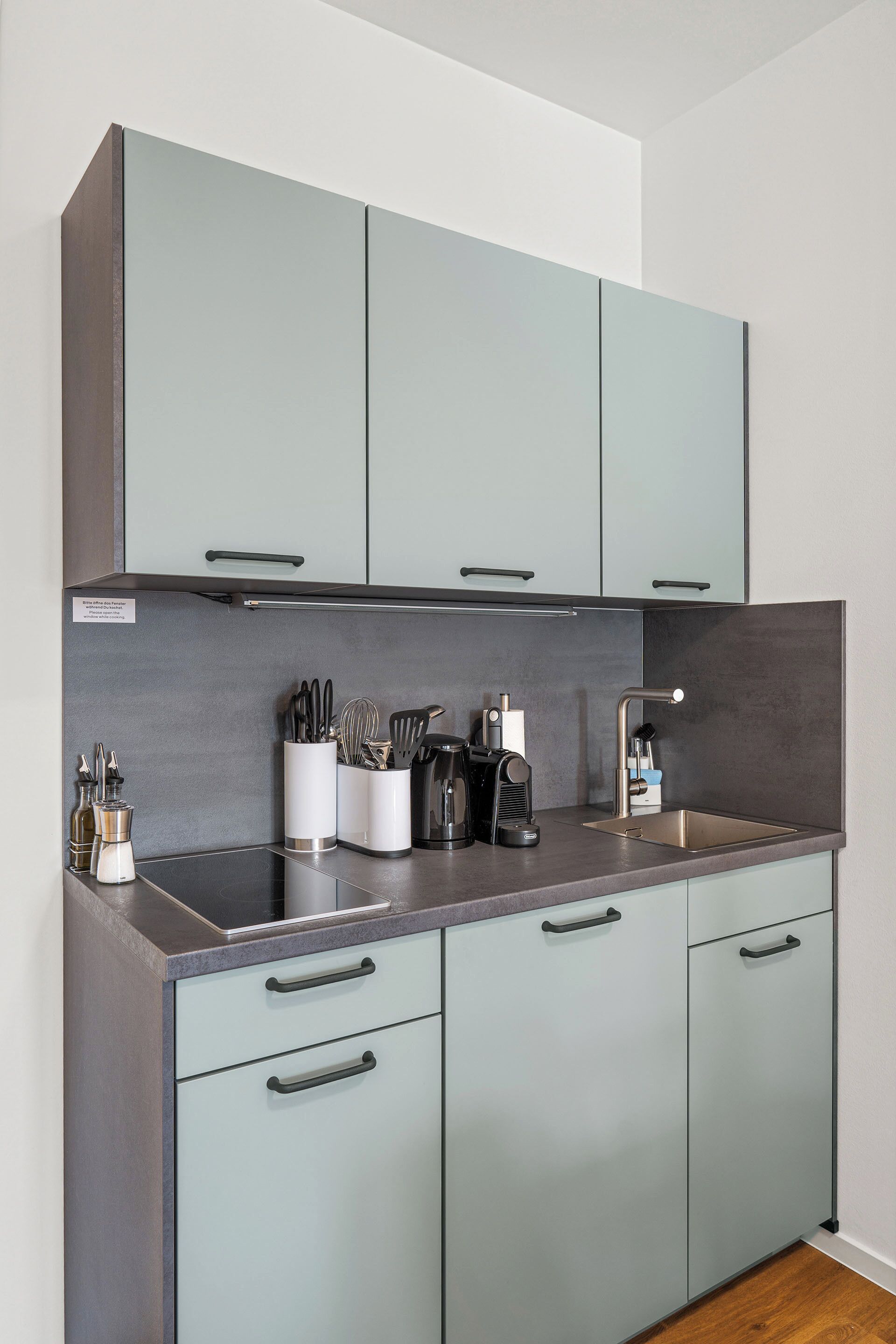 A modern kitchen with grey cabinets, a stainless steel sink, and various kitchen appliances.