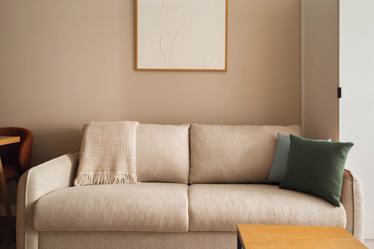 A beige sofa with a textured throw blanket and a green pillow, a wooden coffee table, and a framed abstract artwork on the wall.