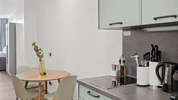Una cocina moderna con una mesa redonda para comer, sillas de color claro y un jarrón con una planta. Se observan armarios con pomos, una cafetera y un soporte para cuchillos en la encimera.
