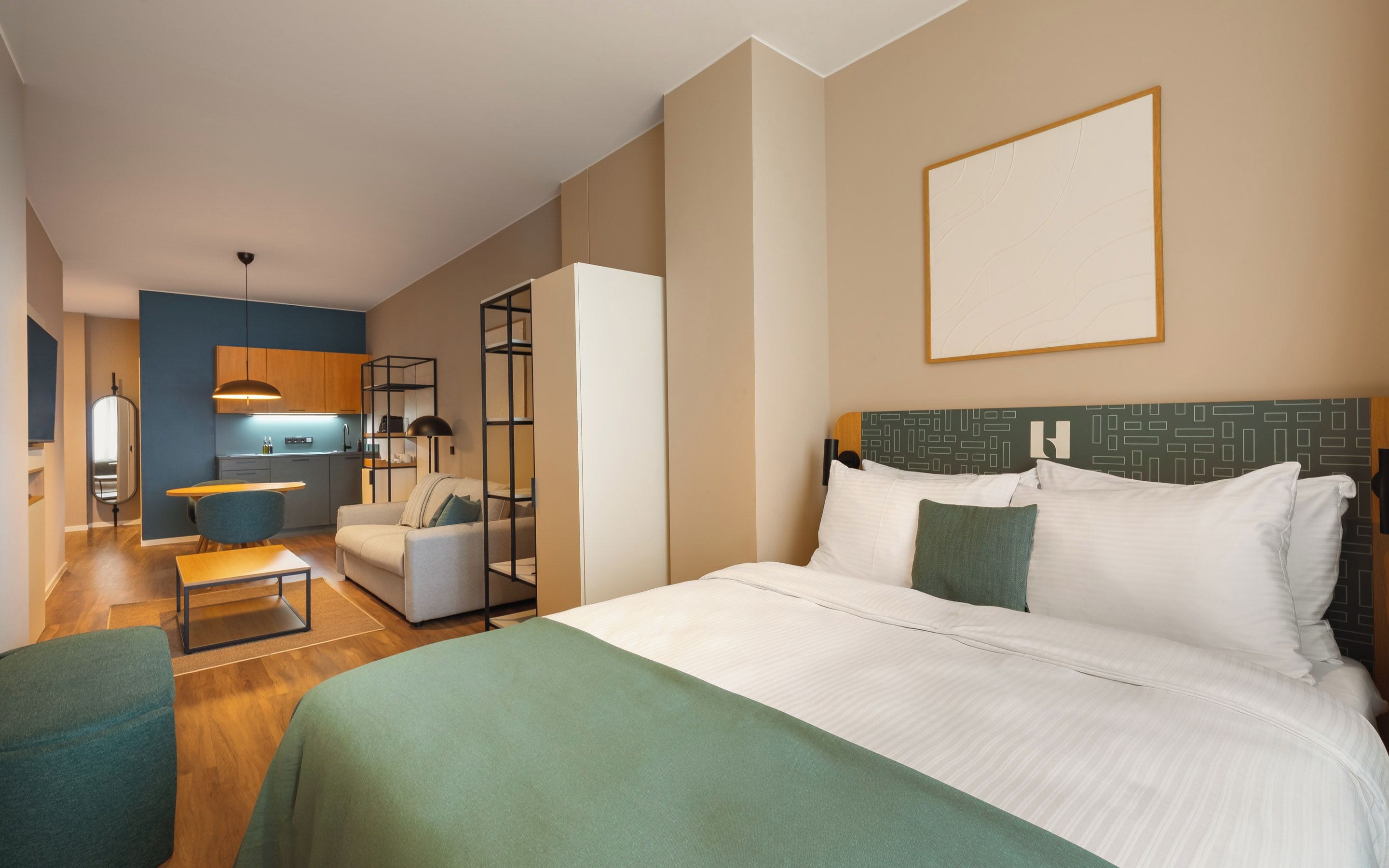 Quarto de hotel com cama grande, sofá, mesa de jantar e cozinha compacta.