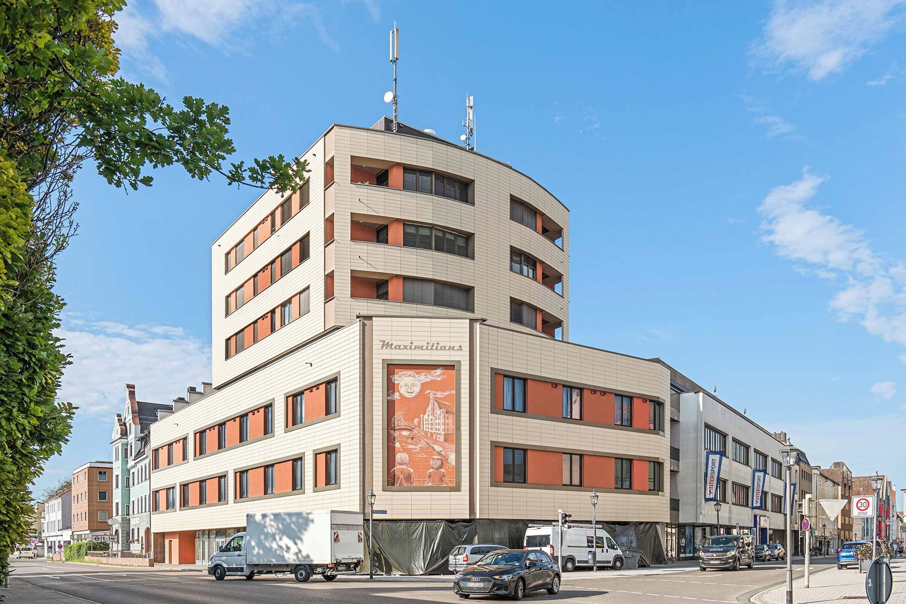 Un edificio de varios pisos con fachada curva, grandes ventanales y un mural destacado en la pared.