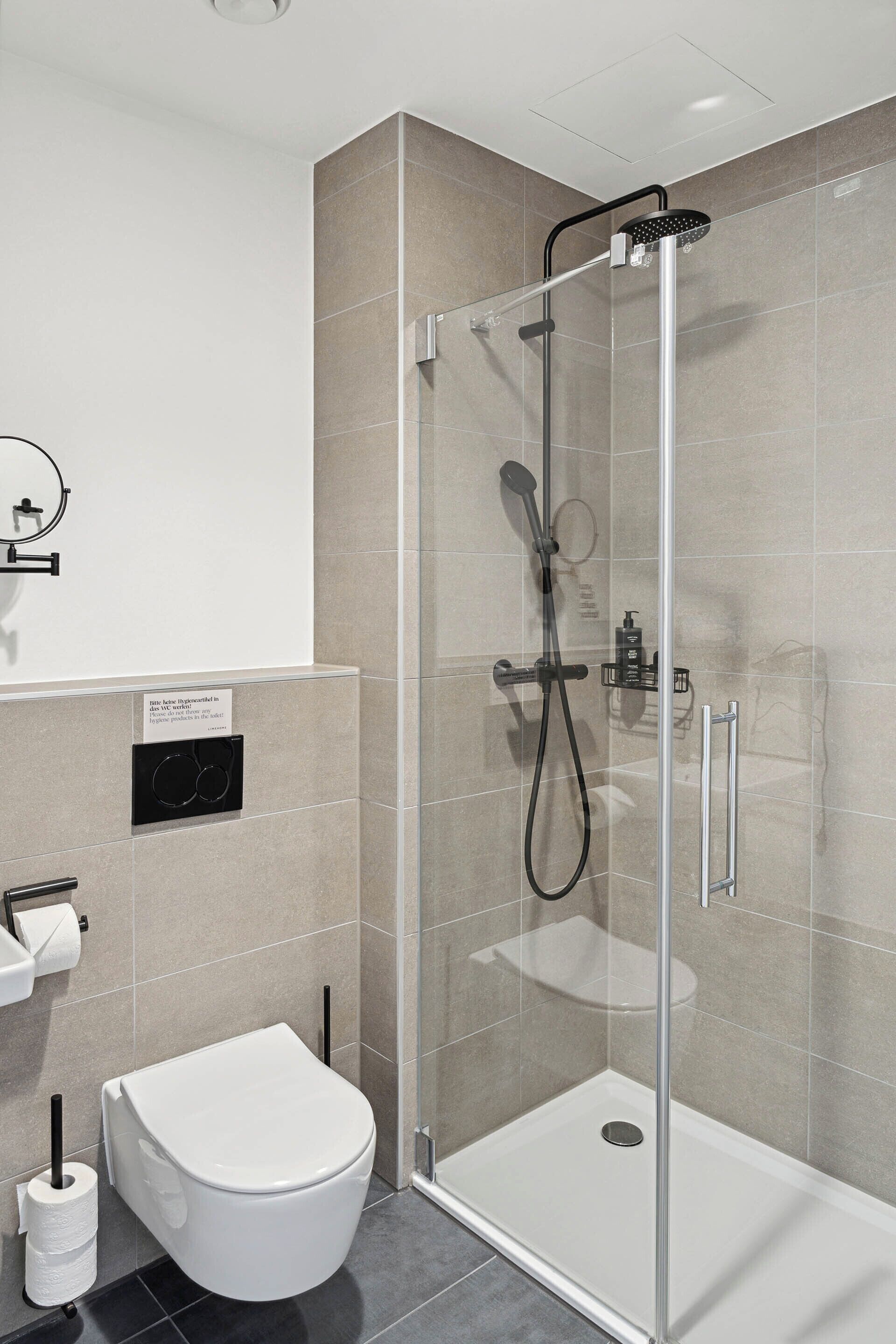 Une salle de bain moderne dotée d’une douche à parois de verre, de toilettes et d’un lavabo.