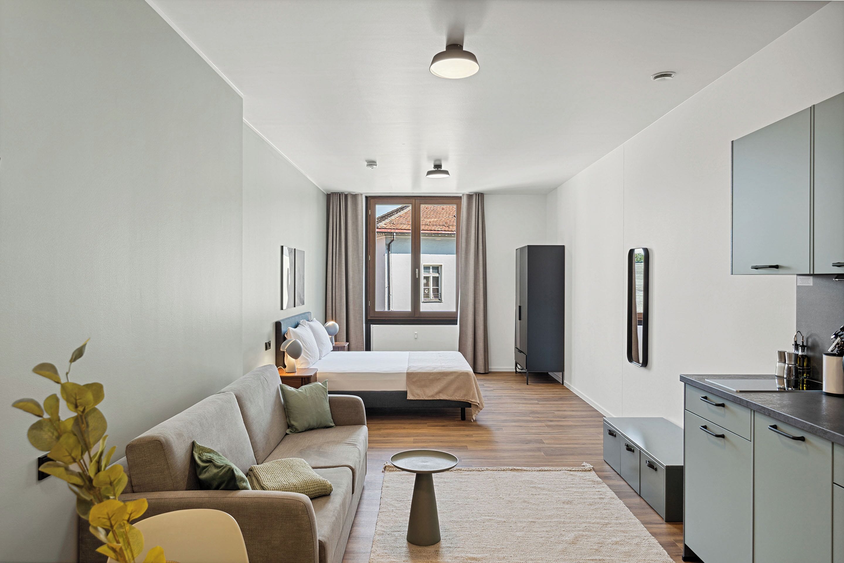 Ett modernt hotellrum med en soffa, en säng, ett litet bord och ett litet kök.