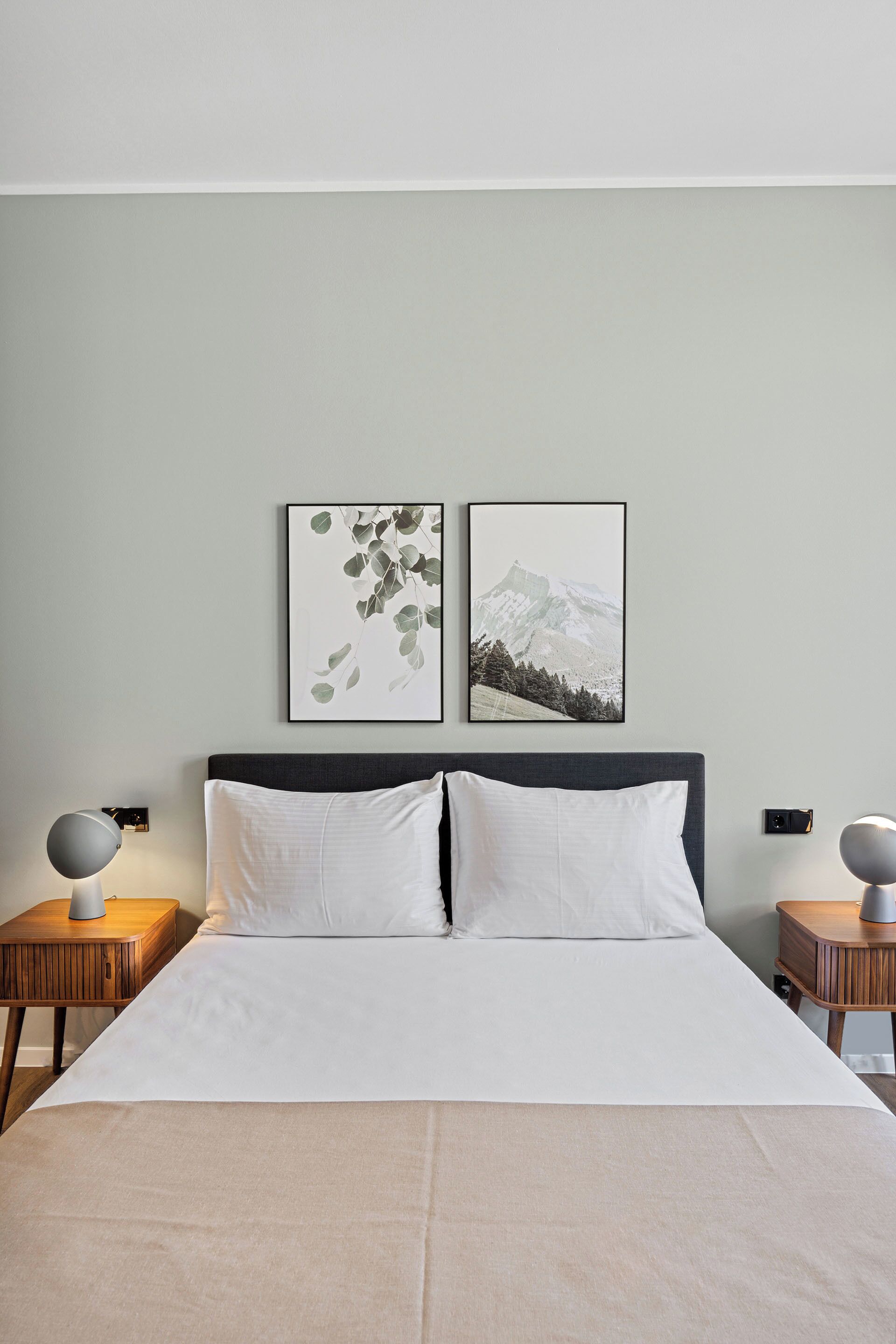 A neatly made bed with white linens, two framed pictures on the wall, and two bedside tables with lamps.