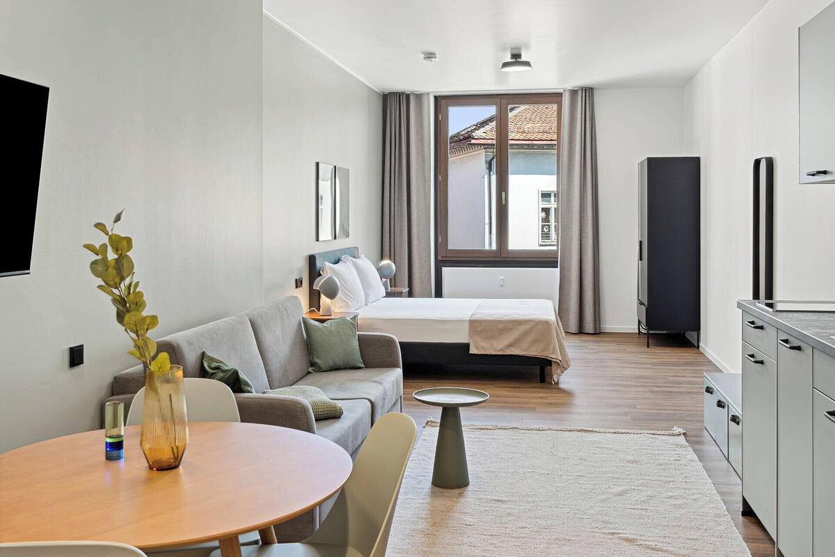 Una habitación moderna y bien iluminada con una mesa de comedor, sillas, un sofá, una cama y una zona de cocina.