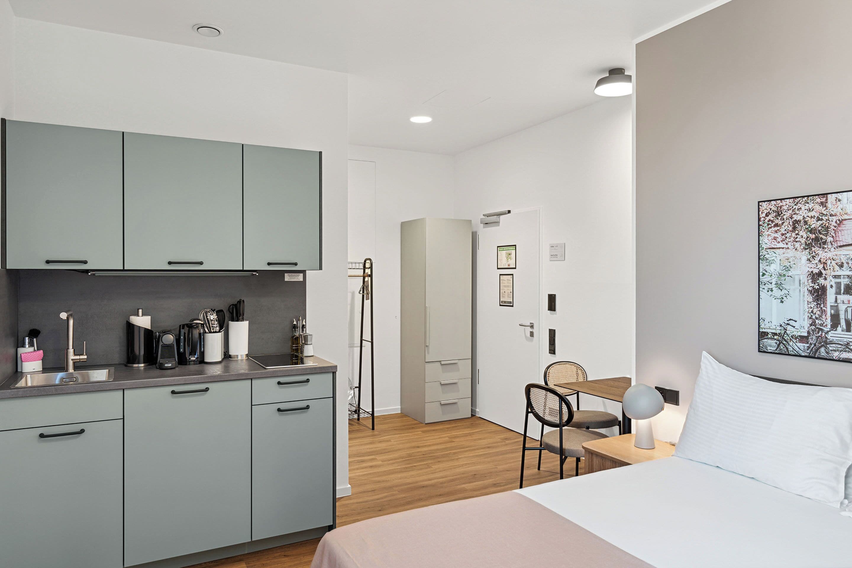 Una habitación de hotel moderna con kitchenette, una cama, un escritorio y una silla.