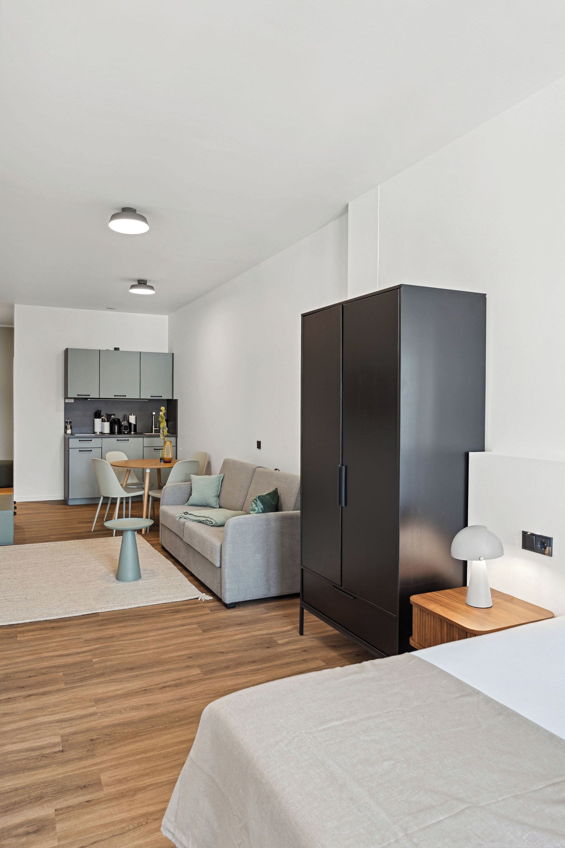 Een moderne, goed verlichte kamer met een bed, een kledingkast, een eethoek en een keuken op de achtergrond.