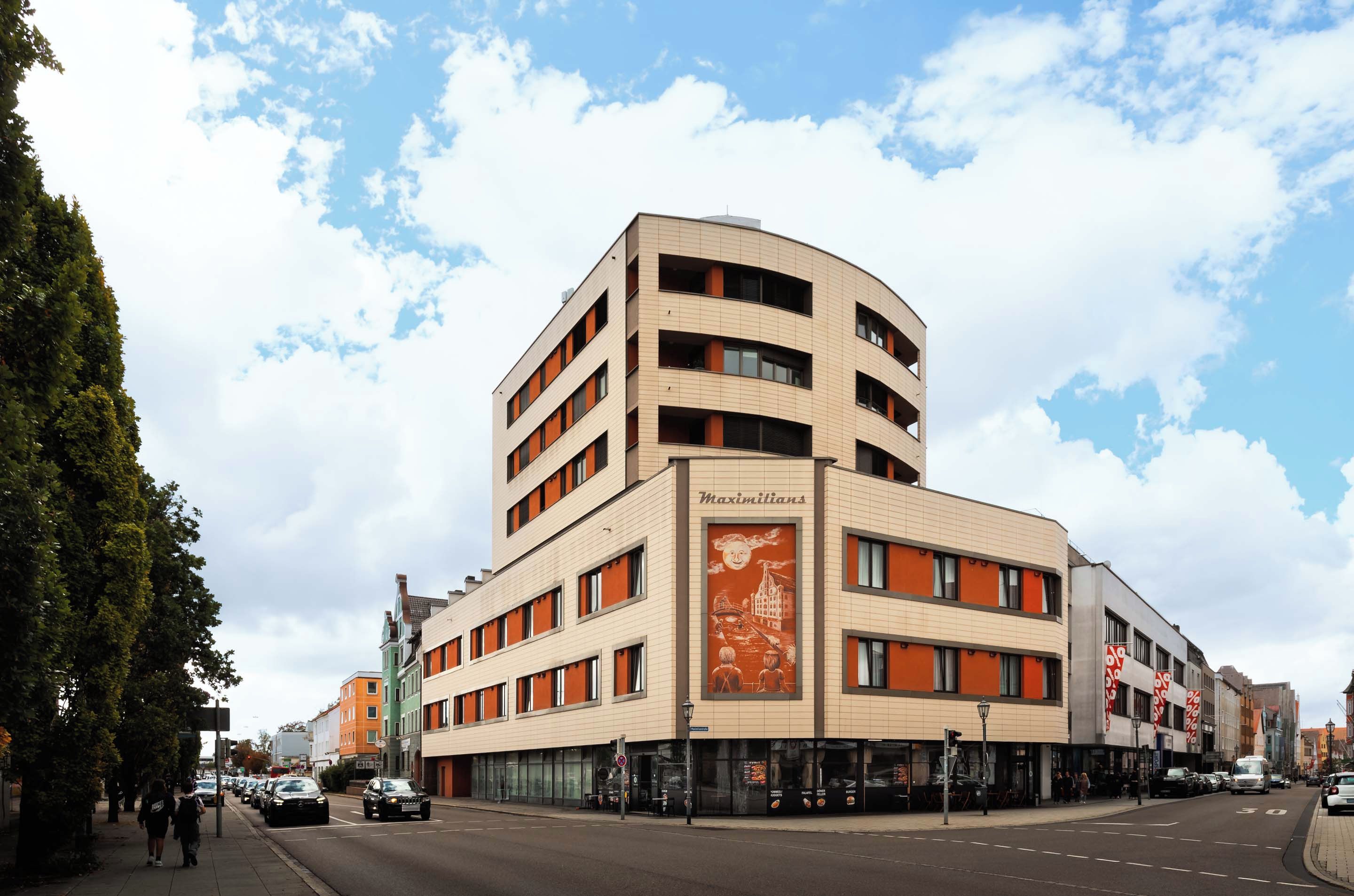 A multi-story building with a curved facade, featuring a prominent sign with a sun illustration and the word 'Maximilians'.