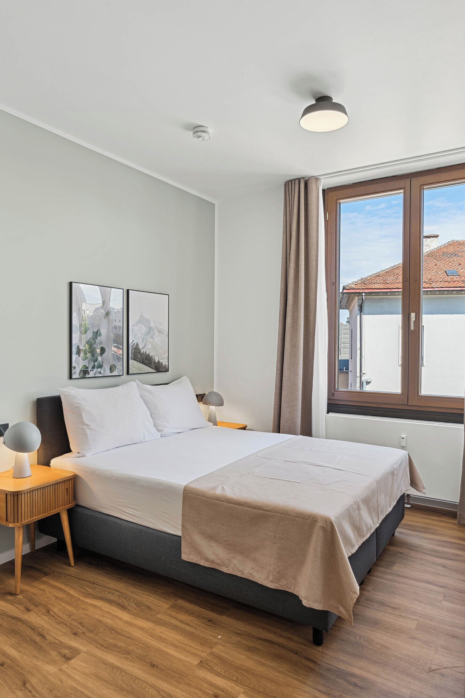 A neatly arranged bedroom with a bed, bedside tables, and a window with curtains.
