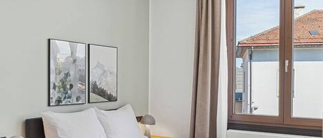 A neatly arranged bedroom with a bed, bedside tables, and a window with curtains.