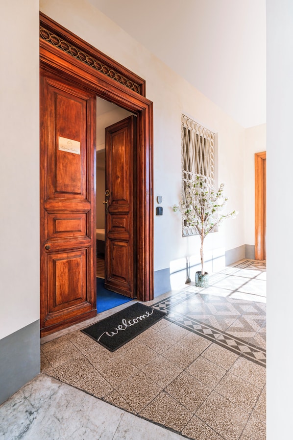 A wooden door with a welcome mat, a potted plant, and a patterned floor. - Elysium Suites Colosseo (Rome)
